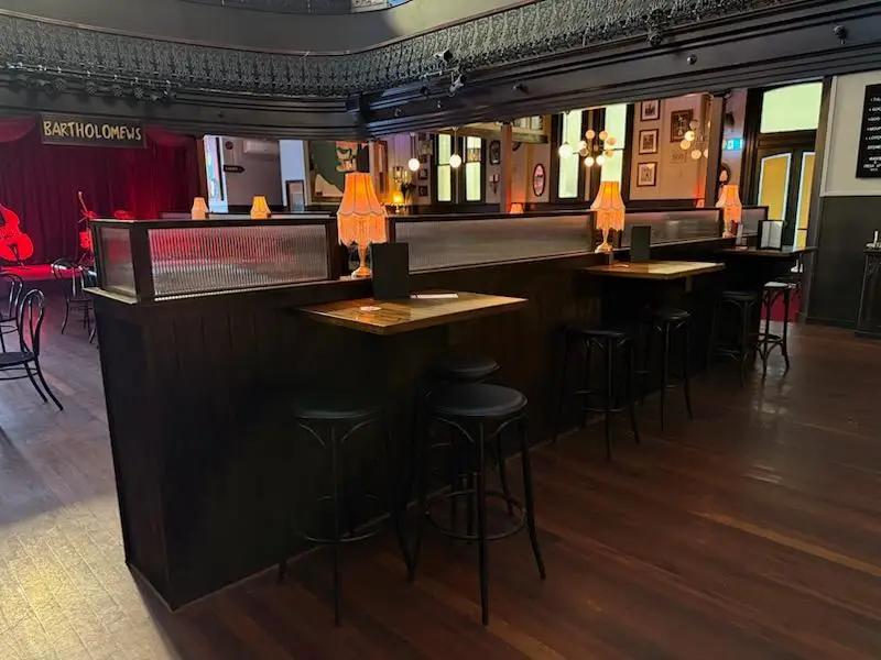 Bar leaner and divider joinery with reeded glass screens and stools in front of a pub stage