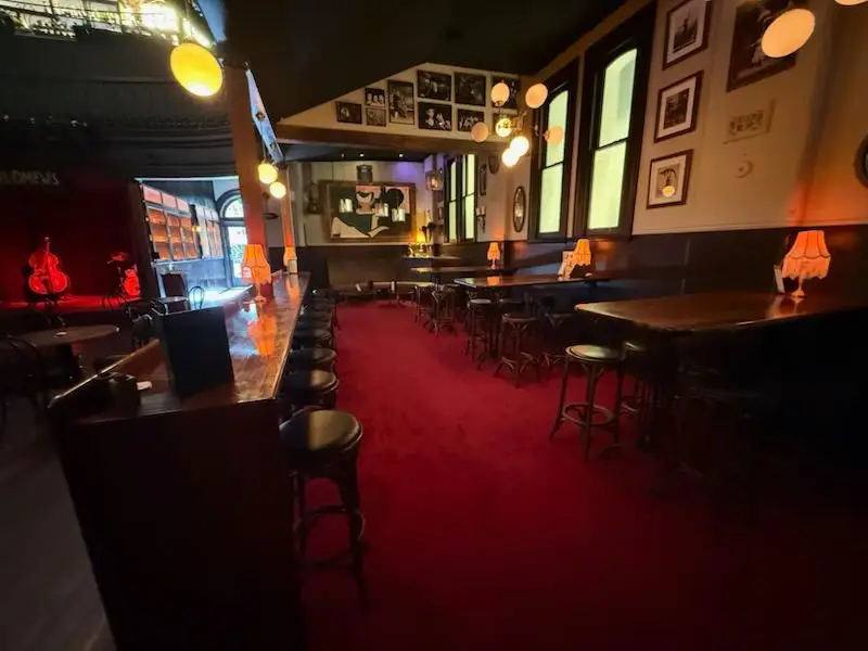 Carpeted pub lounge with a long bar, stools and framed pictures on panelled walls