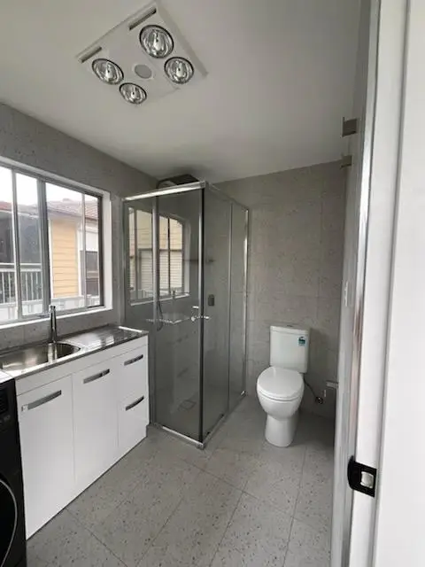 Compact bathroom and laundry with a framed shower screen, toilet suite, bench with laundry tub and a three in one heat lamp