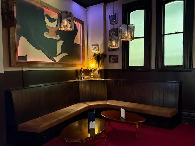 Corner banquette seating with dark timber panelling, oval tables and a large framed artwork above