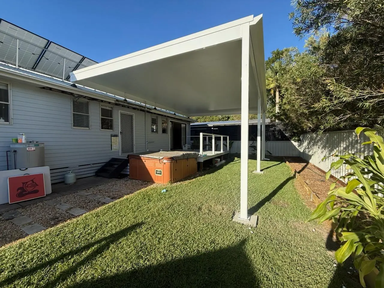 Insulated panel awning over a spa deck behind a weatherboard house, on painted steel posts