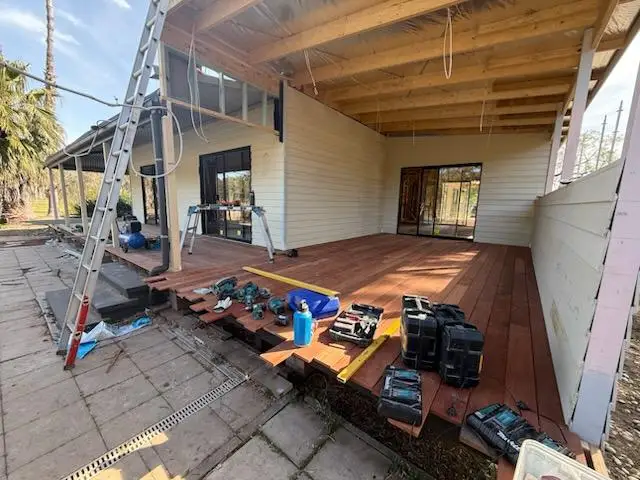 Deck boards part laid under exposed verandah roof framing, with tools and offcuts on the finished section