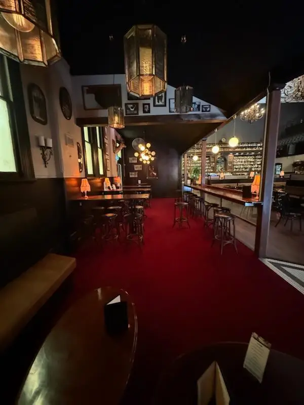 Public bar with high tables, stools and a red carpeted lounge under pendant lighting